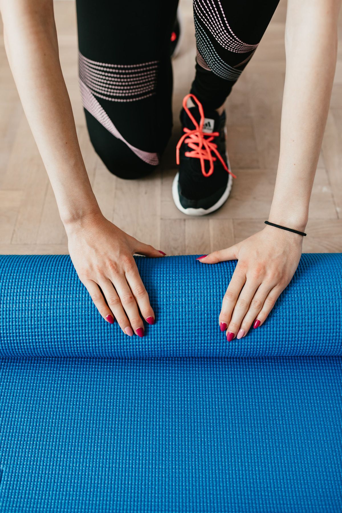 Hands rolling up a yoga mat on a wood floor after a home workout